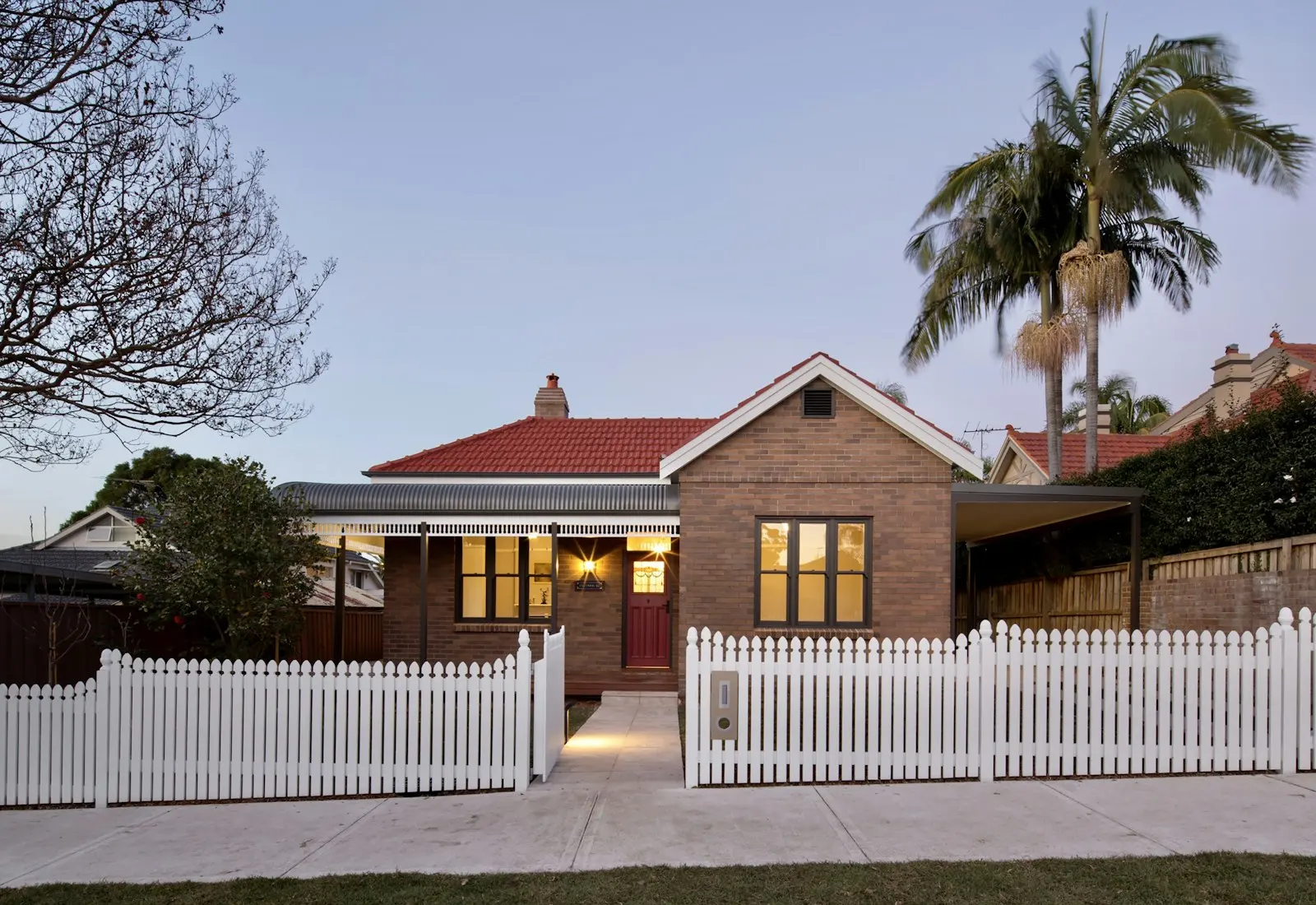 A brick cottage with a white picket fence at dusk